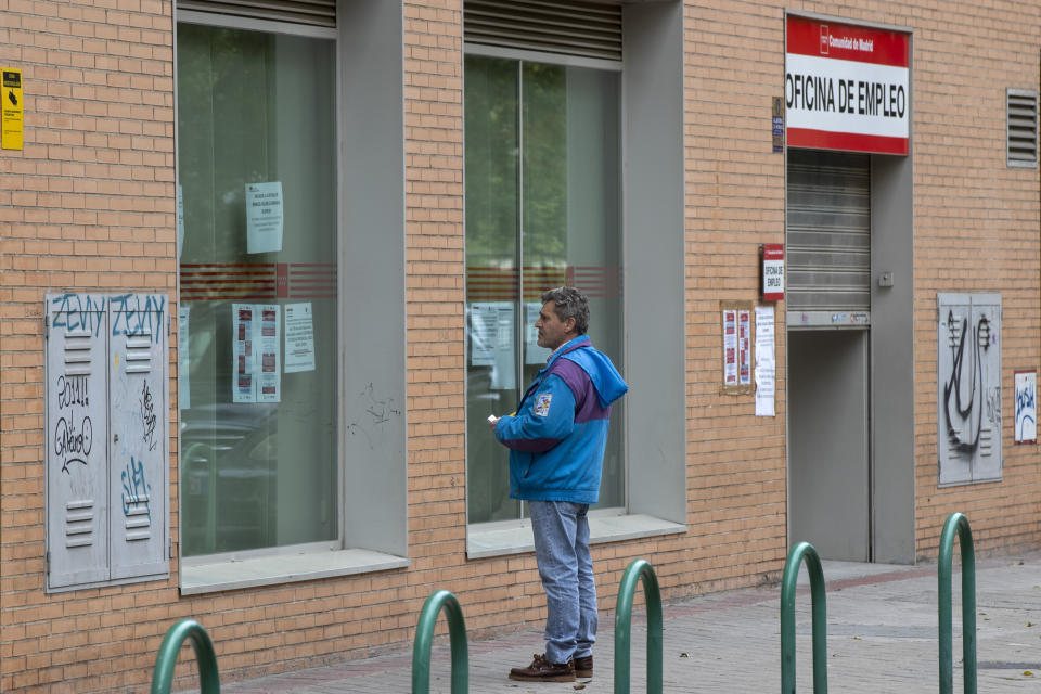 FILE - In this Tuesday, April 28, 2020 file photo, a man looks at notices on the window of an unemployment office in Madrid, Spain. The coronavirus outbreak is straining social safety nets across the globe - and underlining sharp differences in approach between wealthy societies such as the United States and Europe. In Europe, the collapse in business activity is triggering wage support programs that are keeping millions on the job, for now. (AP Photo/Paul White, File)