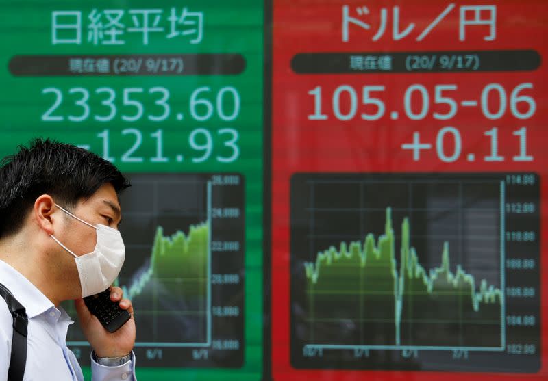 A passerby wearing a protective face masks walks past an electronic board showing Japan's Nikkei average and the exchange rate between Japanese yen against the U.S. dollar, amid the coronavirus disease (COVID-19) outbreak, in Tokyo