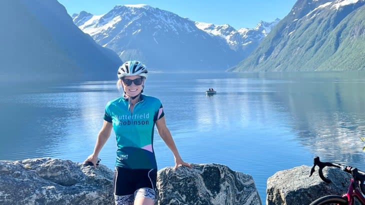 The author wearing a riding kit and cycling helmet, posing against a glassy lake in a Norwegian fjord