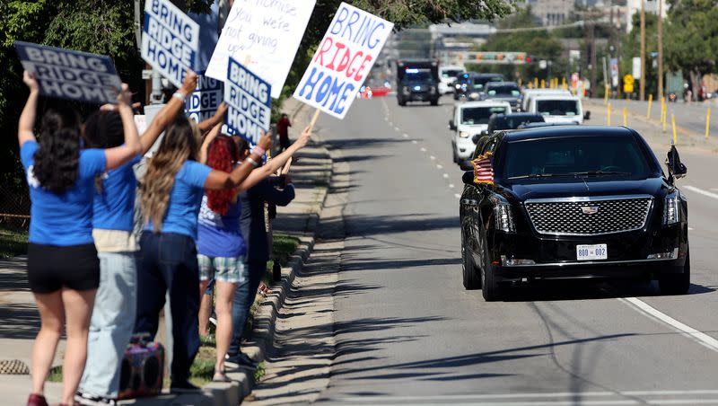 People hold “Bring Ridge Home” signs as a motorcade escorts President Joe Biden to the George E. Wahlen Department of Veterans Affairs Medical Center, where he will deliver remarks, in Salt Lake City on Thursday, Aug. 10, 2023.