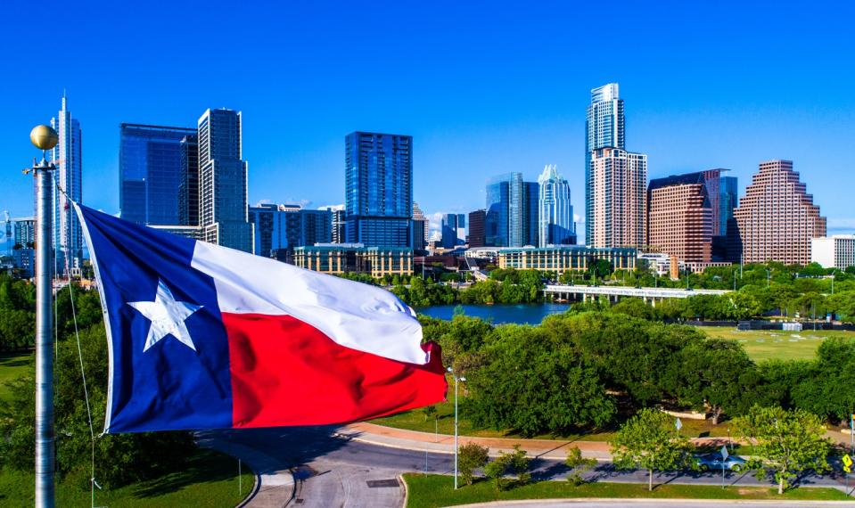 Texas flag flying in front of the Austin skyline.