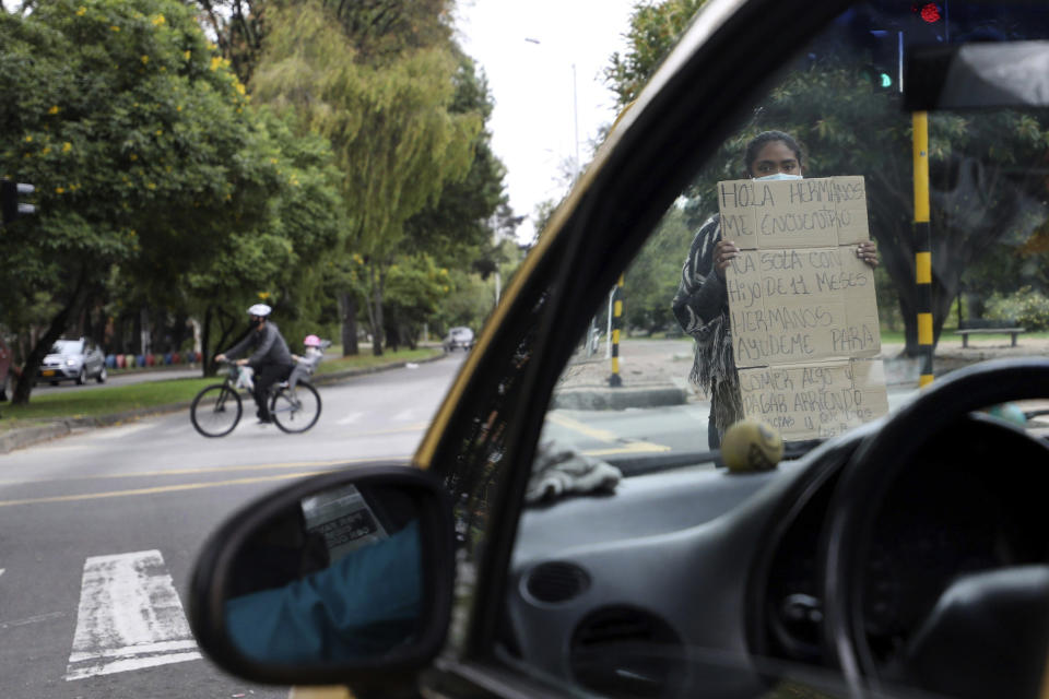 Venezuelan Wuilliamnys Querale, 19, holds up a sign with a handwritten message asking for aid, while standing in a crosswalk in Bogota, Colombia, Tuesday, Feb. 9, 2021. Colombia said Monday it will register hundreds of thousands of Venezuelan migrants and refugees currently in the country without papers, in a bid to provide them with legal residence permits and facilitate their access to health care and legal employment opportunities. (AP Photo/Fernando Vergara)