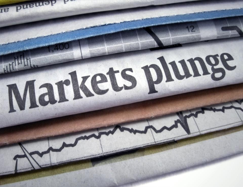 Financial newspapers staggered atop one another, with a single headline visible that reads, Markets plunge.