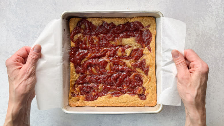 Lifting rhubarb and white chocolate blondies out of baking pan using parchment paper