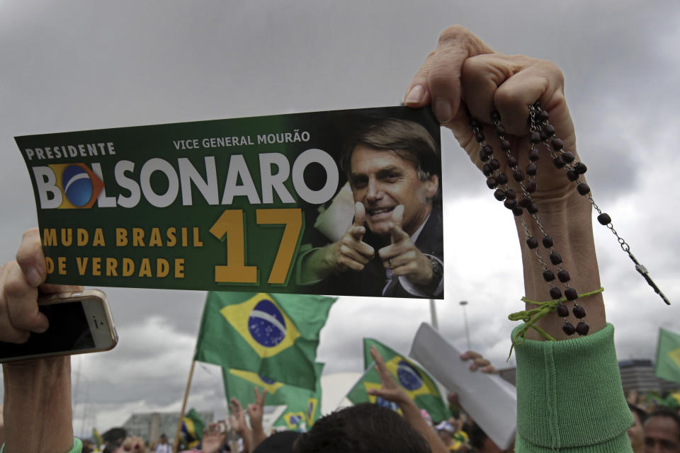 FILE - In this Oct. 21, 2018 file photo, a supporter of presidential candidate Jair Bolsonaro, holds up a bumper sticker supporting her candidate at a campaign rally in Brasilia, Brazil. Bolsonaro, who is leading the polls, has described a Brazil at war: with criminals, with corrupt politicians, with left-wing ideas and, in some ways, with itself. The former army captain’s official platform promises a “decent government, different from everything that landed us in an ethical, moral and fiscal crisis.” (AP Photo/Eraldo Peres, File)