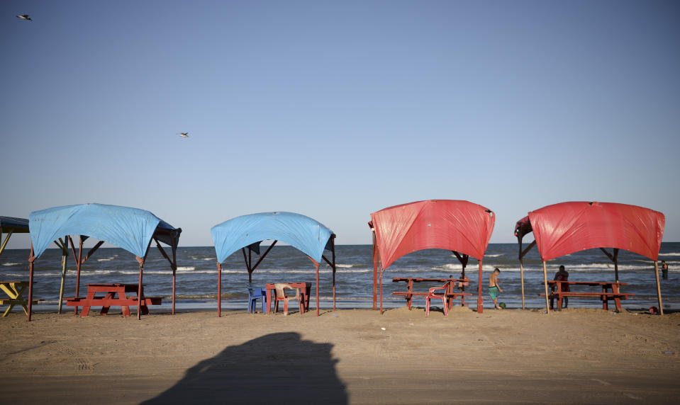 In this Aug. 2, 2019 photo, picnic tables shaded by tarps line the shoreline in Playa Bagdad close to the mouth of the Rio Grande near the border city of Matamoros, Mexico. The only highway that reaches here ends abruptly in a handful of huts populated by beachgoers looking for alcohol and fishermen who might catch sharks one day, and unload cocaine the next. (AP Photo/Emilio Espejel)