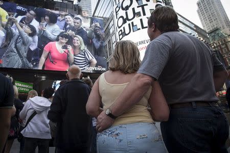 People stand in front of a billboard by Revlon that takes their pictures and displays them on the billboard in Times Square in the Manhattan borough of New York October 13, 2015. REUTERS/Carlo Allegri