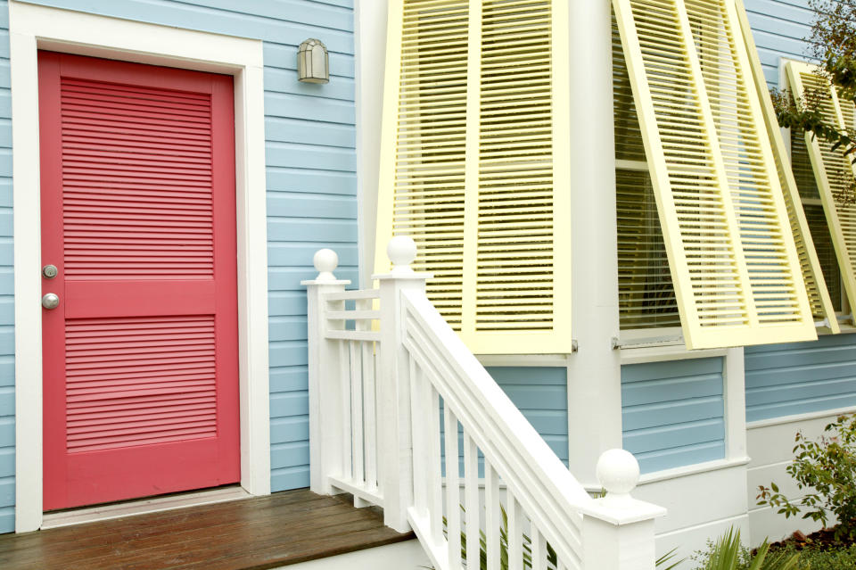 Blue exterior walls with yellow shutters and a red door