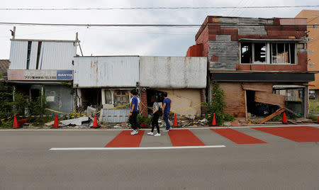 Tourists from Philippines walk past damaged retail premises, near Tokyo Electric Power Co's (TEPCO) tsunami-crippled Fukushima Daiichi nuclear power plant, in Namie town, Fukushima prefecture, Japan May 17, 2018. Picture taken May 17, 2018. REUTERS/Toru Hanai