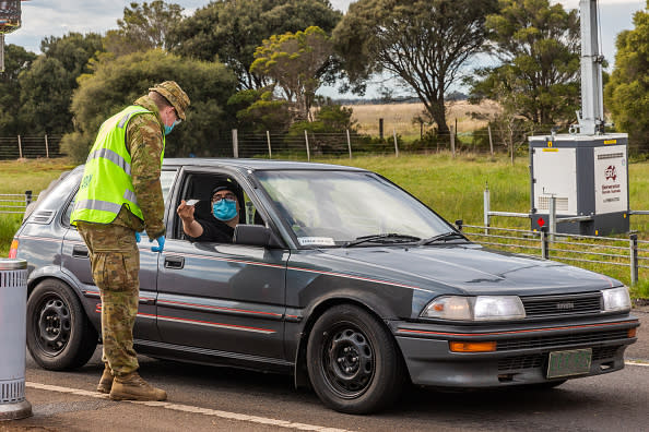 An Australian Defence Force personnel checks the permit and ID of a driver at a checkpoint in Little River for traffic coming from Melbourne into Geelong and the Bellarine Peninsula.