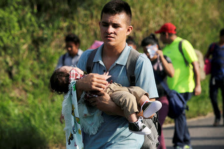 A man carries a child along other Hondurans fleeing poverty and violence, as they move in a caravan toward the United States, in San Pedro Sula, Honduras October 13, 2018. REUTERS/Jorge Cabrera