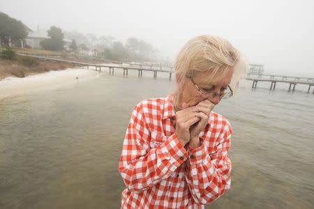 Shirley Walker reacts to seeing unidentified debris washed up behind her home near where rescue crews search waters for a missing helicopter around the Navarre Bridge, east of Pensacola, Florida March 11, 2015. REUTERS/Michael Spooneybarger