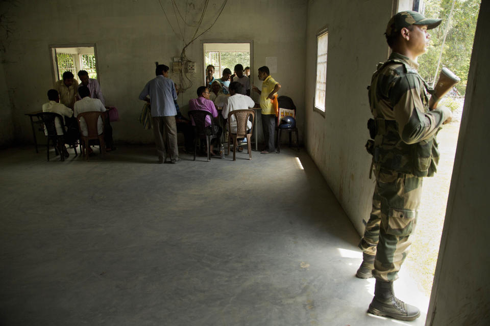 A soldier stands guard as people, whose names or whose family members names were left out in the National Register of Citizens (NRC) draft, collect forms to file appeals in Mayong, 45 kilometers (28 miles) east of Gauhati, India, Friday, Aug. 10, 2018. A draft list of citizens in Assam, released in July, put nearly 4 million people on edge to prove their Indian nationality. Nativist anger churns through Assam, just across the border from Bangladesh, with many believing the state is overrun with illegal migrants. (AP Photo/Anupam Nath)
