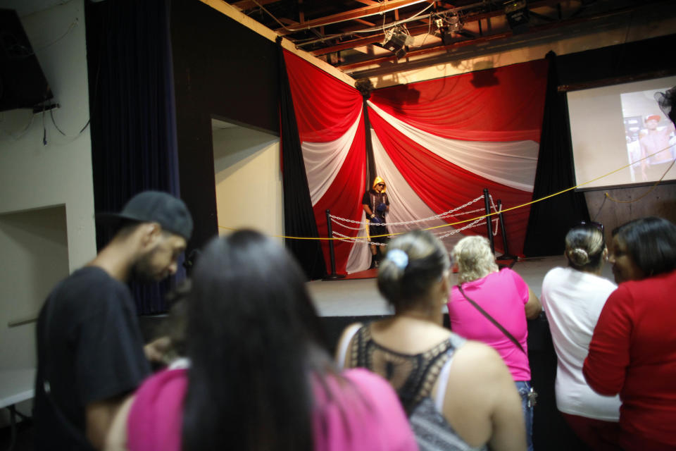 People attend the wake of boxer Christopher Rivera, whose body is propped up in a fake boxing ring, at the community recreation center within the public housing project where he lived in San Juan, Puerto Rico, Friday, Jan. 31, 2014. Elsie Rodriguez, vice president of the Marin funeral home, explained that Rivera had asked his family that in the case of his death, he wanted his funeral to make reference to his boxing career. Rivera was shot to death on Sunday. (AP Photo/Ricardo Arduengo)