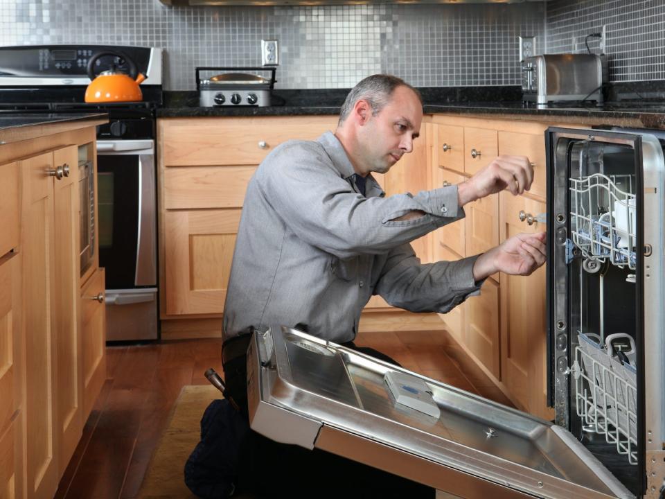Repairman fixing dishwasher in kitchen.