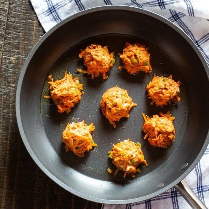 A handful of sweet potato latkes cooking in a frying pan.