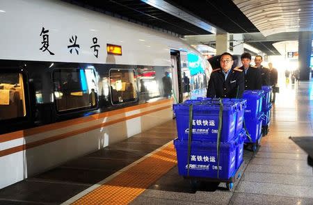 Staff members carry express boxes next to a Fuxing bullet train during a test operation for an express service, jointly offered by China Railway Express and Chinese delivery company SF Express, to deliver goods between Beijing and Shanghai with Fuxing bullet trains for the upcoming Singles Day online shopping festival, at Beijing South Railway Station in Beijing, China November 9, 2017. Picture taken November 9, 2017. REUTERS/Stringer