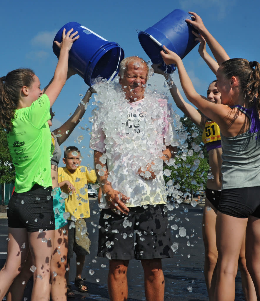 Two individuals pour ice water on a person for an ALS Ice Bucket Challenge as others watch