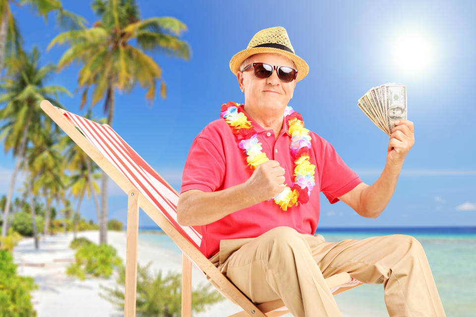 An older man sitting at the beach holding cash.
