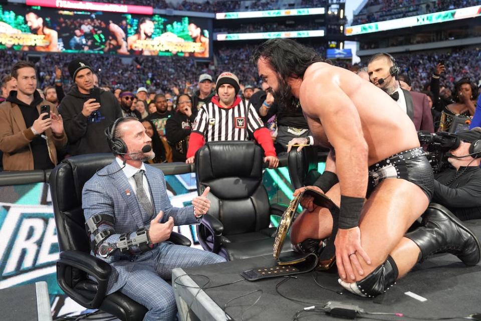 Drew McIntyre, kneeling on the commentator's table has a face off with a seated CM Punk after WWE World Championship win during Night Two of WrestleMania 40 at Lincoln Financial Field on April 7, 2024 in Philadelphia, Pennsylvania.