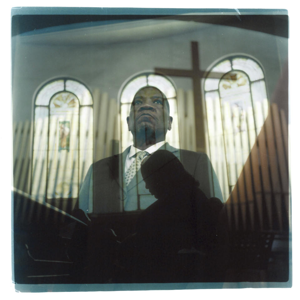 In this double exposure darkroom print made from two film negatives, a portrait of Rev. Jimmie Hardaway Jr. looking out from the altar of Trinity Baptist church is layered with a photo of a parishioner bowing her head in prayer during a service Sunday, Aug. 20, 2023, in Niagara Falls, N.Y. The decision Hardaway has made to carry a pistol on him during church services is a distinctly American one. And it spotlights rising friction between the assertion of two very American principles: the right to worship and the right to own guns. "I'm really not free if I have to sit here and worry about threats to a congregation," says Hardaway, one of several religious leaders who sued New York officials last fall after lawmakers restricted guns in houses of worship. He notes the similarities between Trinity's worshippers and those at a historic Black church in Charleston S.C., where a mass shooter killed nine people in 2015. "I'm really not free," says Hardaway, whose city struggles with one of the state's highest rates of violent crime, "if I know that there's someone who can do harm and I can't do anything to protect them." (AP Photo/David Goldman)