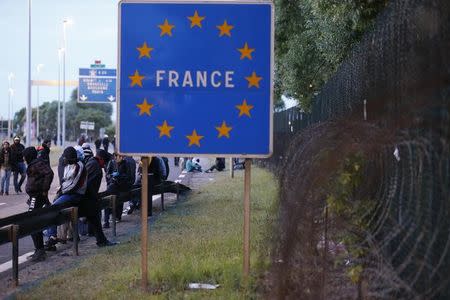 Migrants sit on a road barrier near a fence with coils of razor-wire in Coquelles, near Calais,France, July 30, 2015. REUTERS/Pascal Rossignol