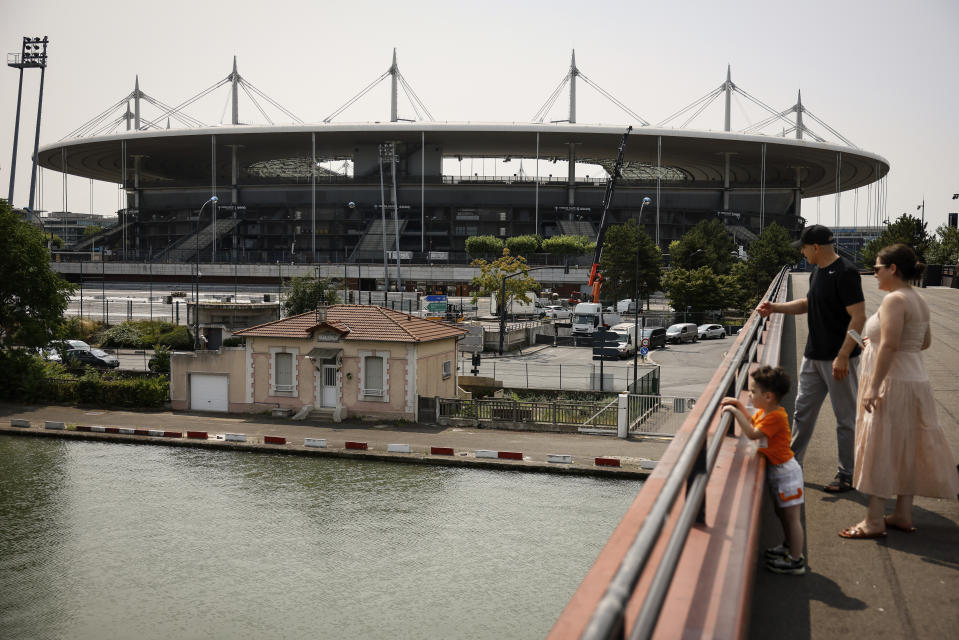 A family looks at the Canal Saint-Denis with the Stade de France stadium in background, Monday, July 10, 2023 in Saint-Denis, north of Paris. The stadium will host the athletics and para athletics and Rugby Sevens in the Paris 2024 games. (AP Photo/Thomas Padilla, File)