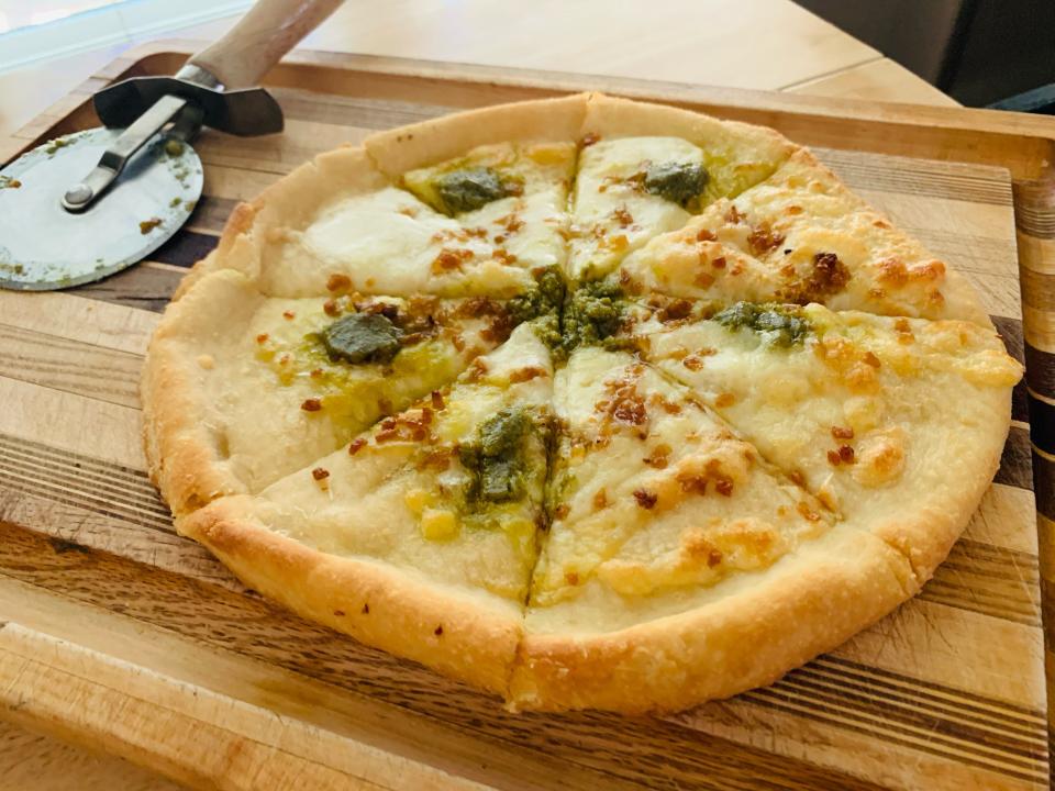 cooked Trader Joe's garlic and pesto pizza on cutting board with pizza slicer beside it