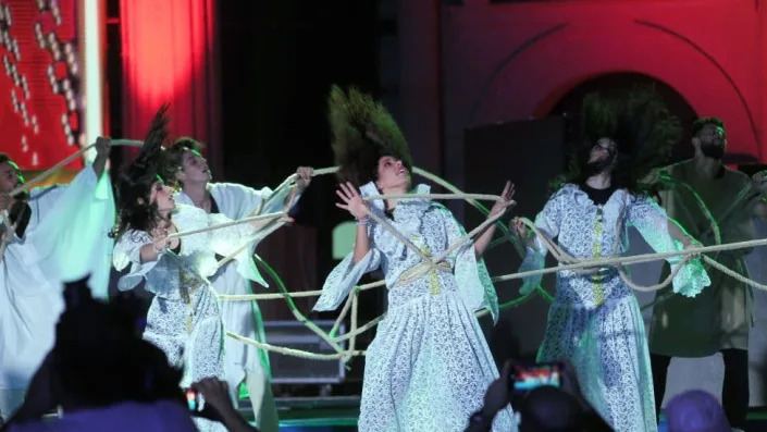 A group of performers dancing. Their hair is blowing and they are wearing white dresses.