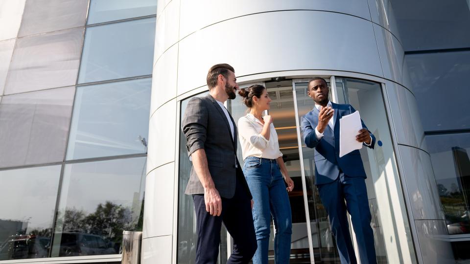 Portrait of a happy salesman selling a car to a couple at the dealership Ã¢Â€Â“ lifestyle concepts.