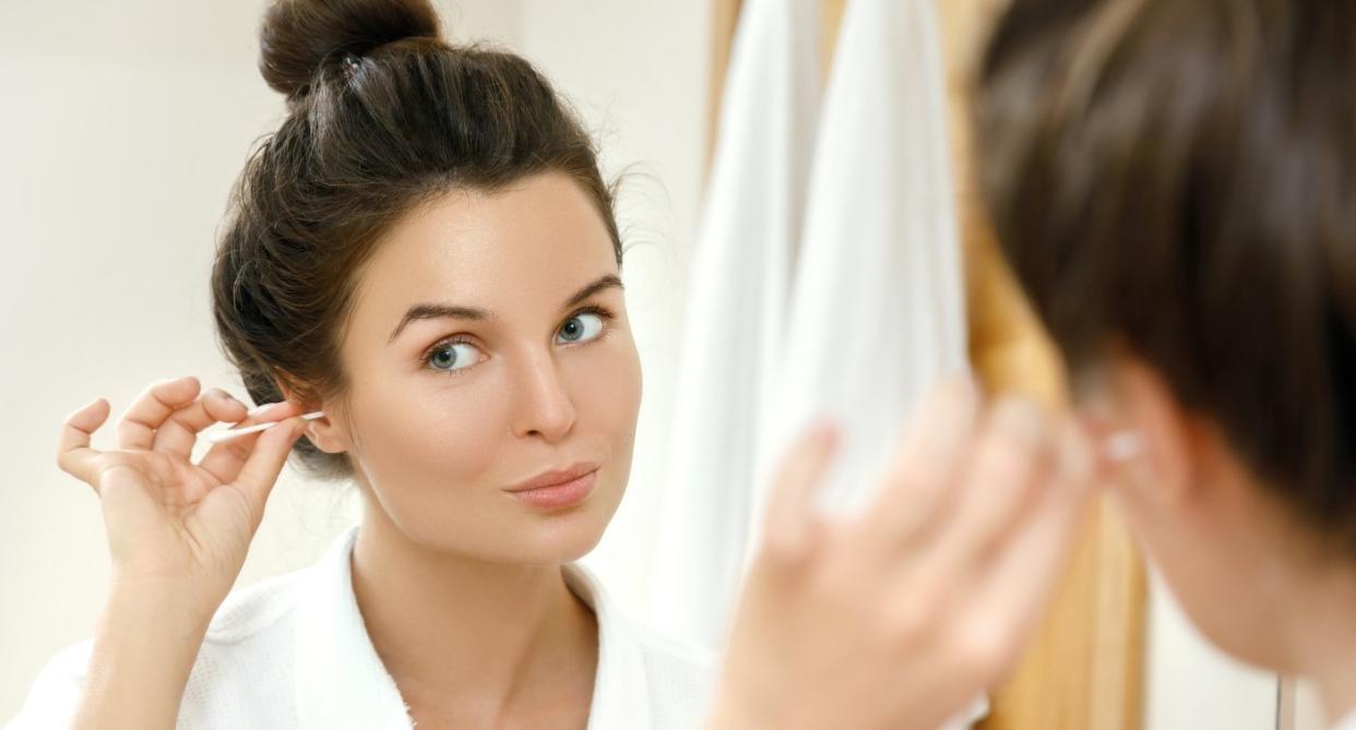 Woman poking ear with cotton bud to illustrate causes of hearing loss 