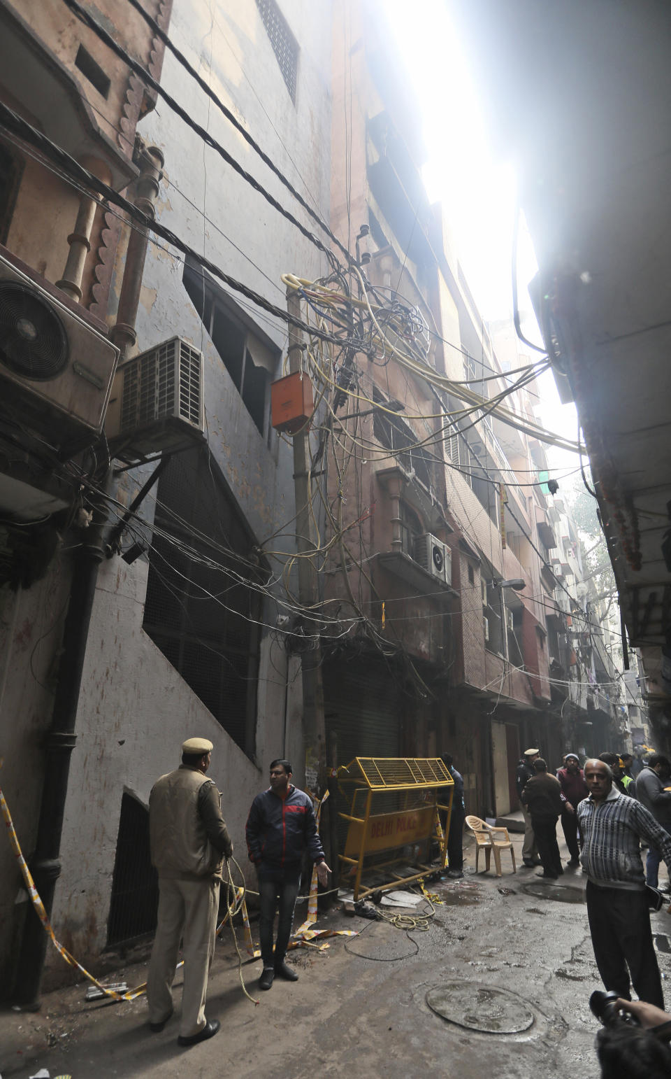 Policemen and neighbors stand in front of a ilnl-fated building which caught fire on Sunday, in New Delhi, India, Monday, Dec. 9, 2019. Authorities say an electrical short circuit appears to have caused a devastating fire that killed dozens of people in a crowded market area in central New Delhi. Firefighters fought the blaze from 100 yards away because it broke out in one of the area's many alleyways, tangled in electrical wire and too narrow for vehicles to access. (AP Photo/Manish Swarup)