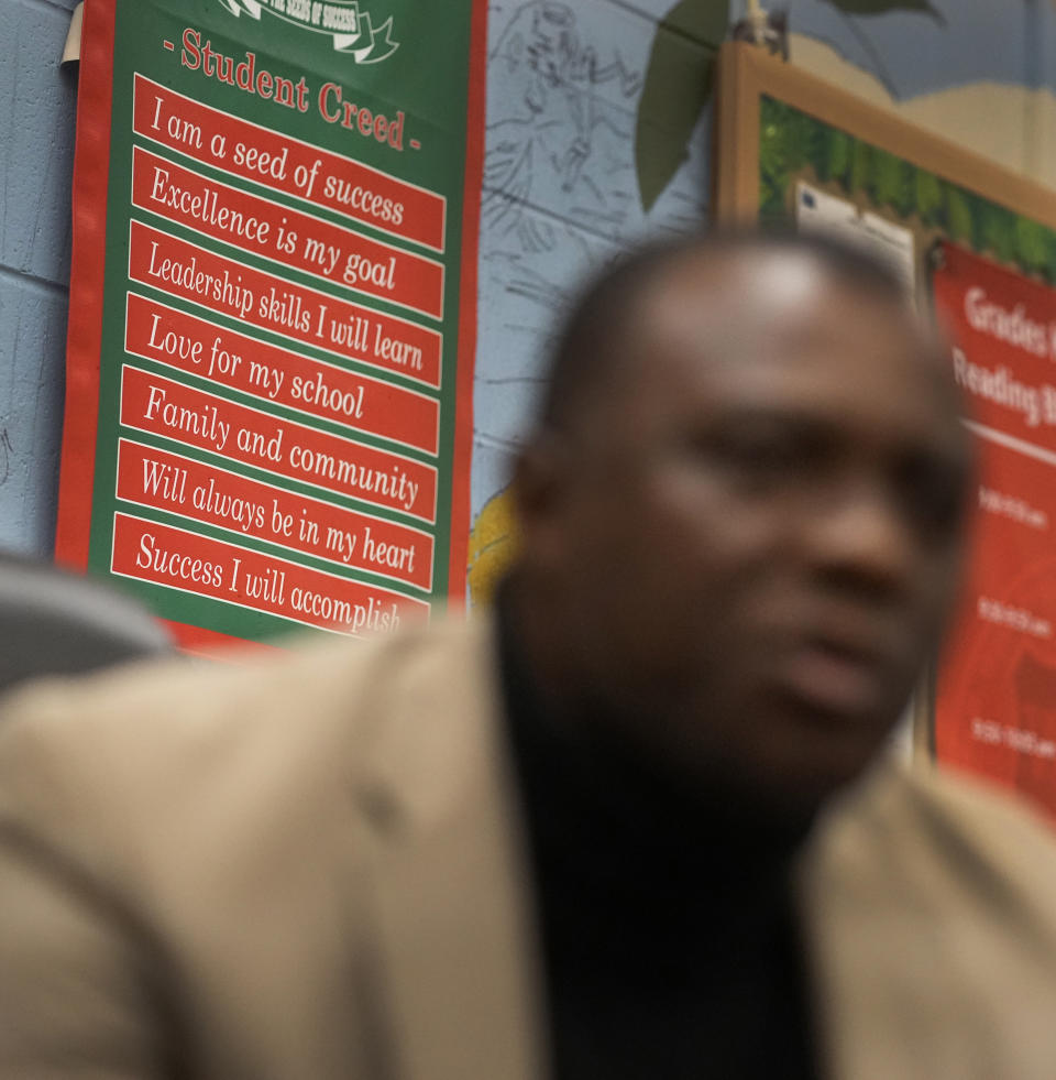 The Wells Preparatory Elementary School Student Creed hangs on the wall behind principal Vincent Izuegbu on Friday, March 8, 2024, in Chicago. At Wells Preparatory Elementary on the South Side, just 3% of students met state reading standards in 2021. Last year, 30% hit the mark. Federal relief allowed the school to hire an interventionist for the first time, and teachers get paid to team up on recovery outside working hours. (AP Photo/Charles Rex Arbogast)