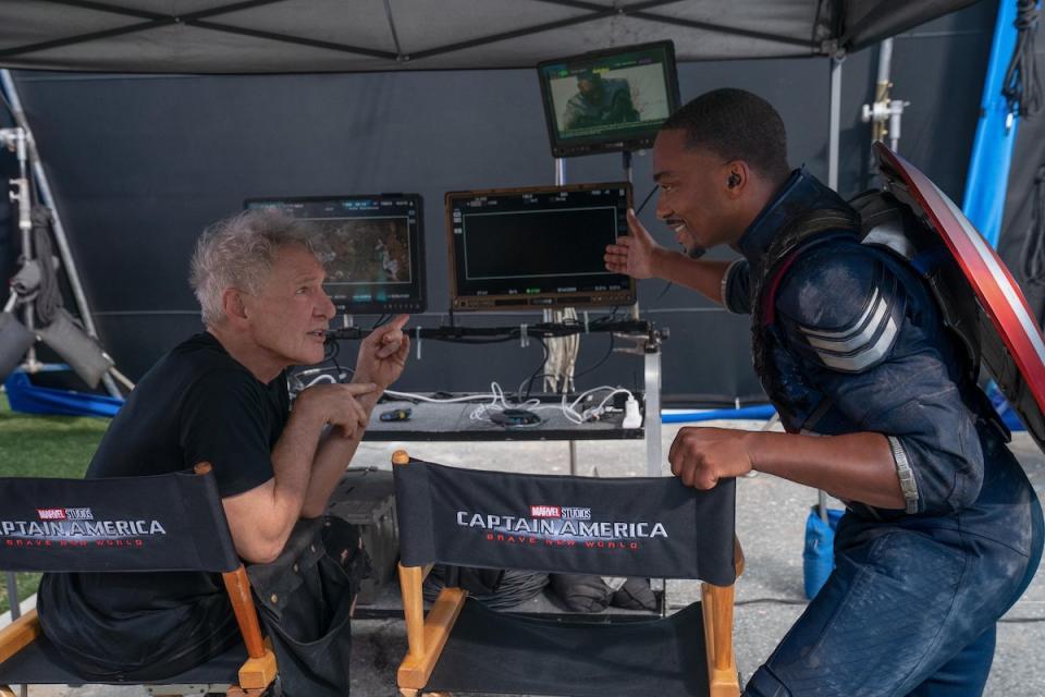 Harrison Ford in a chair talks to Anthony MAckie in front of monitors on the set of Captain America: Brave New World