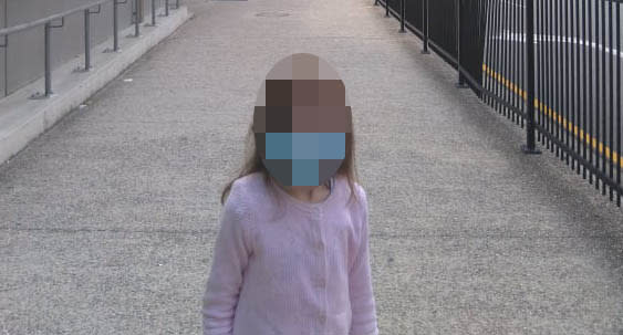 A young girl with symptoms of a brain disorder stands outside Queensland Children's Hospital wearing a mask. Source: Supplied