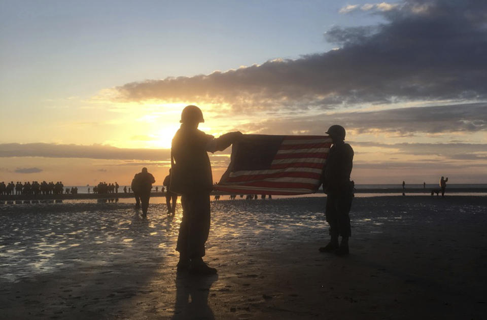 Re-enactors hold an American flag at sunrise as part of events to mark the 75th anniversary of D-Day on Omaha Beach in Vierville-sur-Mer, Normandy, France, Thursday, June 6, 2019. World leaders are gathered Thursday in France to mark the 75th anniversary of the D-Day landings. (Maxence Piel via AP)