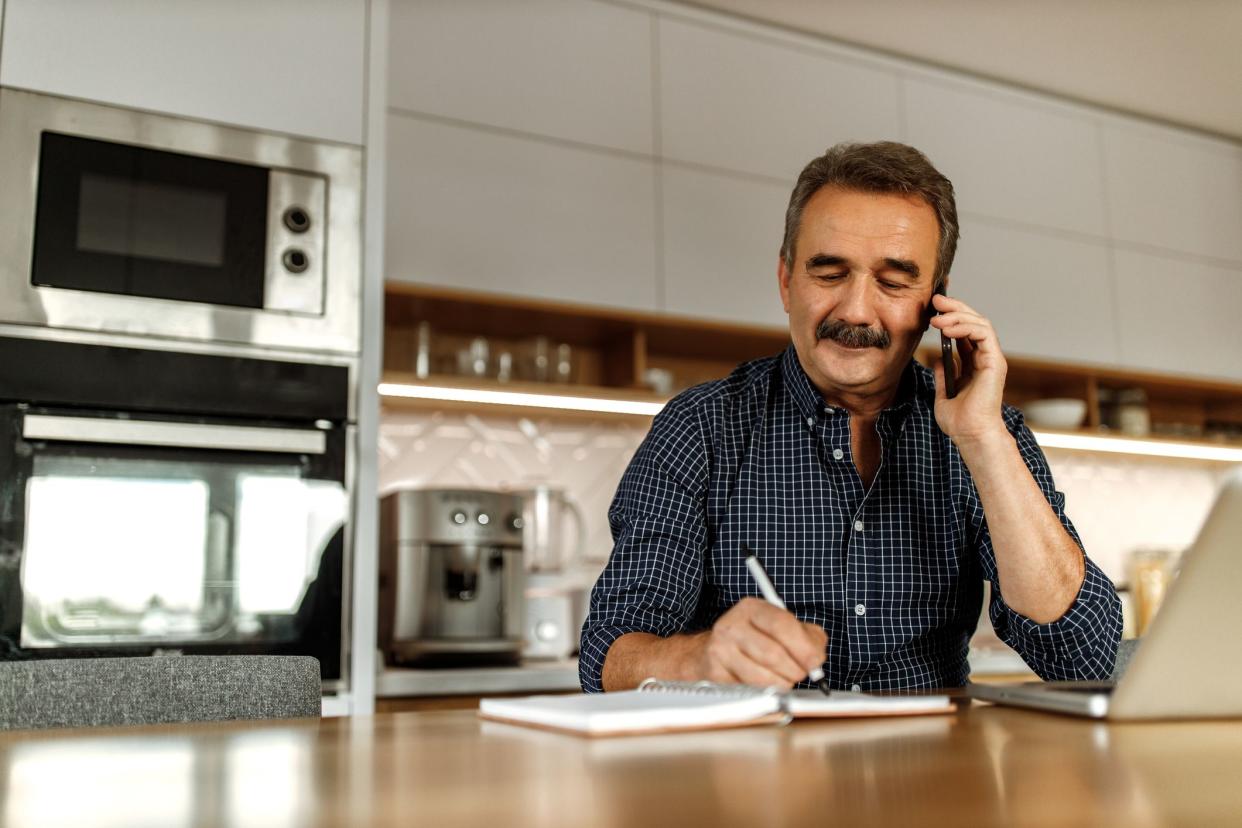 Adult man making phone call, while reading and writing some words in his notebook.