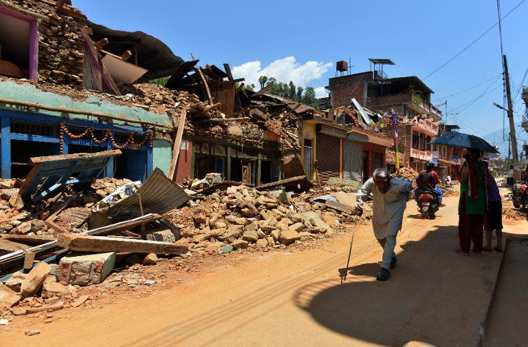 Nepalese people walk past damaged houses at Trishuli in Nuwakot on May 4, 2015 following the earthquake in April