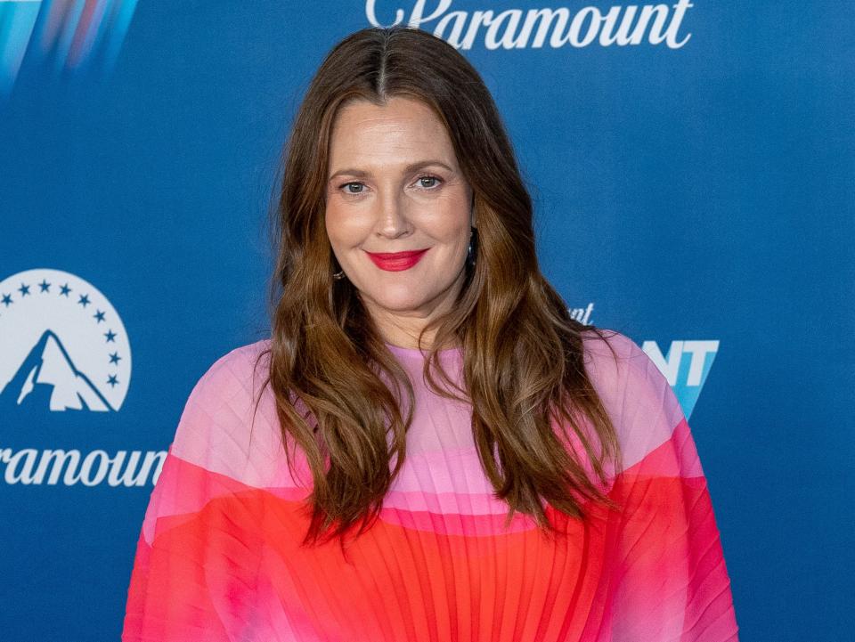 Drew smiling in a red and pink dress in front of a backdrop.