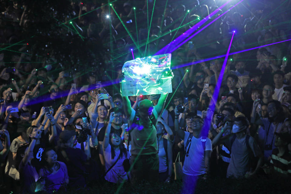 Protesters focus the laser pointers to a newspaper as they try to burn it, during a rally to demonstrate against the arrests of people caught in possession of laser pointers that police classified as offensive weapons because of their ability to harm the eyes in Hong Kong, Wednesday, Aug. 7, 2019. Hong Kong is facing its "most severe situation" since its handover from British rule in 1997 following weeks of demonstrations and the central government is considering what measures to take next, the head of Beijing's Cabinet office responsible for the territory said Wednesday. (AP Photo/Kin Cheung)