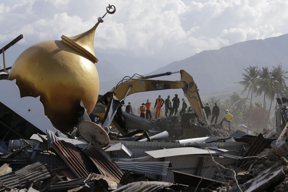 In this Saturday, Oct. 6, 2018, file photo, rescuers stand beside a toppled mosque as recovery efforts continue in the earthquake-hit Balaroa neighborhood in Palu, Central Sulawesi, Indonesia. (AP Photo/Aaron Favila, File)