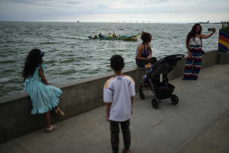 Residents gather on a seawall as passengers ride a boat on Lake Maracaibo, in Maracaibo, Venezuela, Thursday, Aug. 10, 2023. The lake has turned into a polluted wasteland, with crude leaking from rusting oil platforms and cracked pipelines. (AP Photo/Ariana Cubillos)