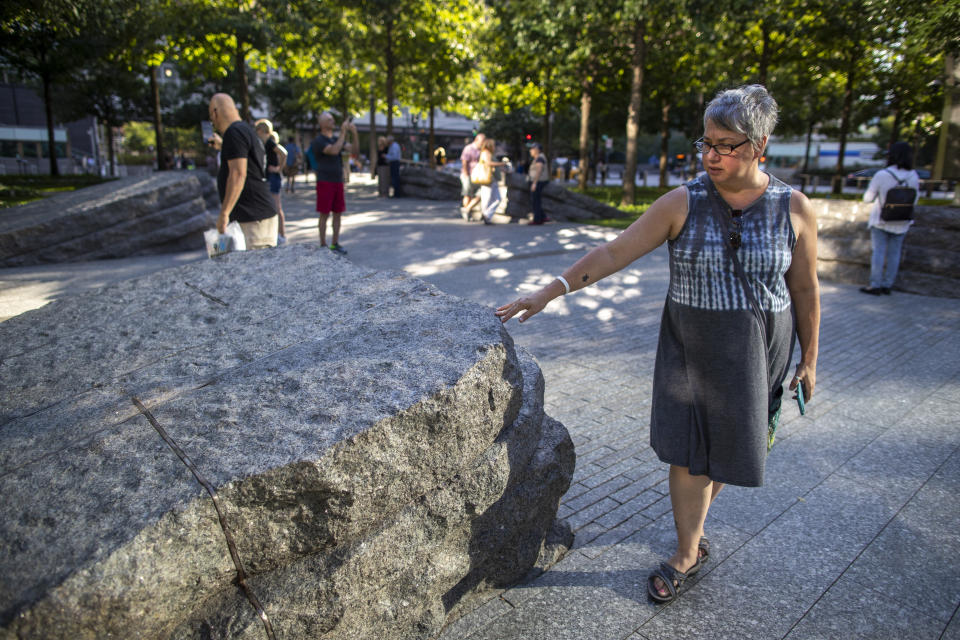 In this Thursday, Aug. 29, 2019, photo a visitor touches one of the granite slabs at the 9/11 Memorial Glade at the National September 11 Memorial & Museum in New York. When the names of nearly 3,000 Sept. 11 victims are read aloud Wednesday, Sept. 11 at the World Trade Center, a half-dozen stacks of stone will quietly salute an untold number of people who aren’t on the list. The granite slabs were installed on the memorial plaza this spring. They recognize an initially unseen toll of the 2001 terrorist attacks: firefighters, police and others who died or fell ill after exposure to toxins unleashed in the wreckage. (AP Photo/Mary Altaffer)