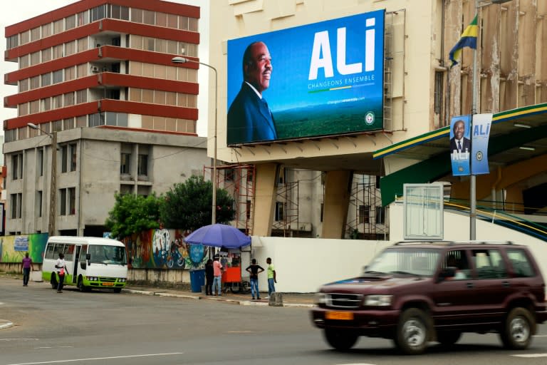 People go about with their daily life as they stand under an electoral poster campaign picturing current Gabonese President and presidential candidate Ali Bongo Ondimba in Libreville, on August 13, 2016 during the first day of the Presidential campaign
