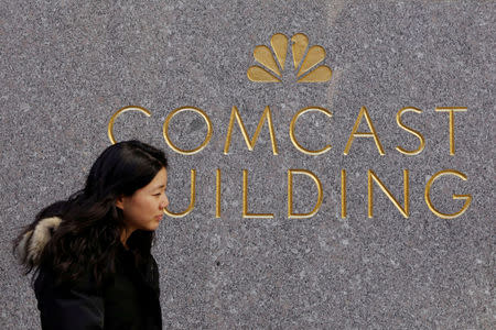 FILE PHOTO: A woman walks past the NBC and Comcast logos on 30 Rockefeller Plaza in midtown Manhattan in New York, U.S., February 27, 2018. REUTERS/Lucas Jackson/File Photo