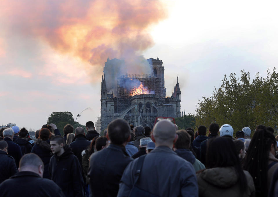 FILE - In this Monday, April 15, 2019 file photo, people watch as flames and smoke rise from Notre Dame cathedral in Paris. On Friday, April 19, 2019, The Associated Press has found that stories circulating on the internet that a Muslim woman in Paris was arrested for planning a terrorist attack at the cathedral, days before the fire, are untrue. Paris police investigators have said they think an electrical short-circuit most likely caused the fire. (AP Photo/Thibault Camus)