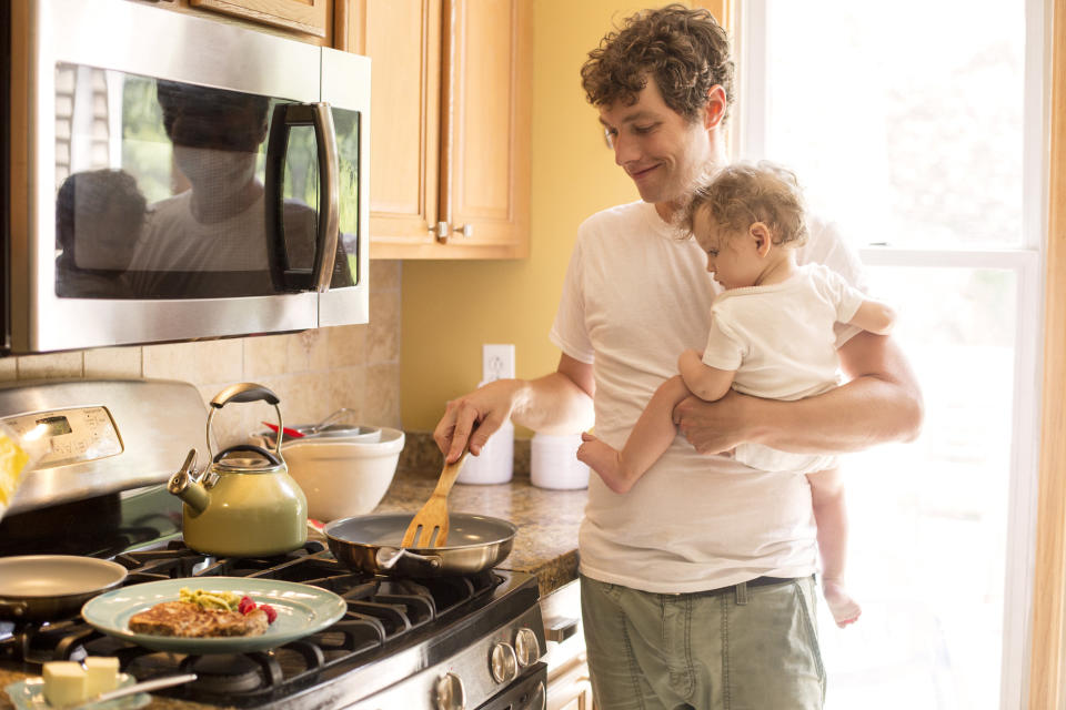 a man cooking and holding a baby