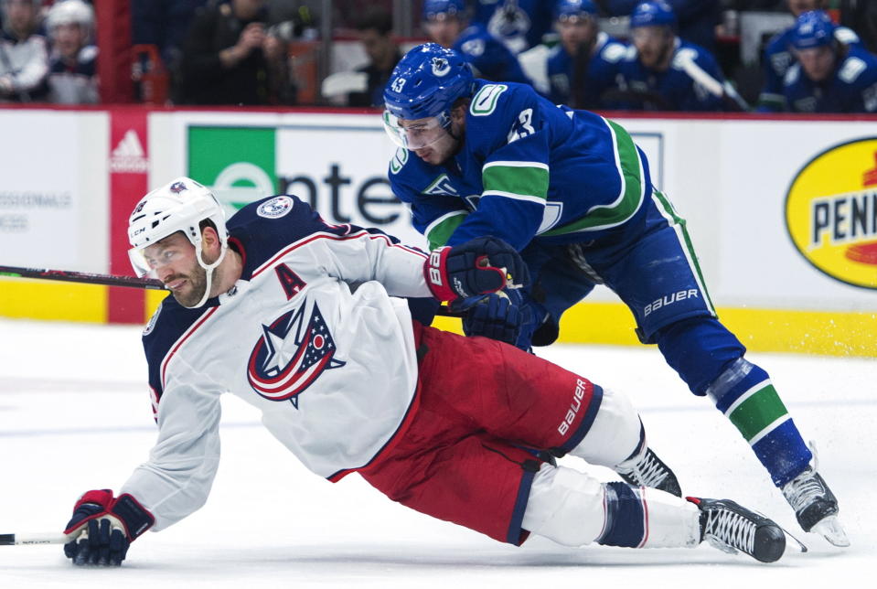 Vancouver Canucks defenseman Quinn Hughes (43) fights for control of the puck with Columbus Blue Jackets center Boone Jenner (38) during the first period of an NHL hockey game, in Vancouver, British Columbia, Sunday, March 8, 2020. (Jonathan Hayward/The Canadian Press via AP)
