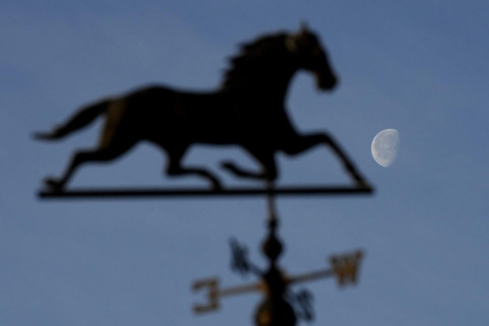 The moon rises beyond a weather vane on a barn as horses workout at Churchill Downs Monday, April 29, 2024, in Louisville, Ky. The 150th running of the Kentucky Derby is scheduled for Saturday, May 4. (AP Photo/Charlie Riedel)