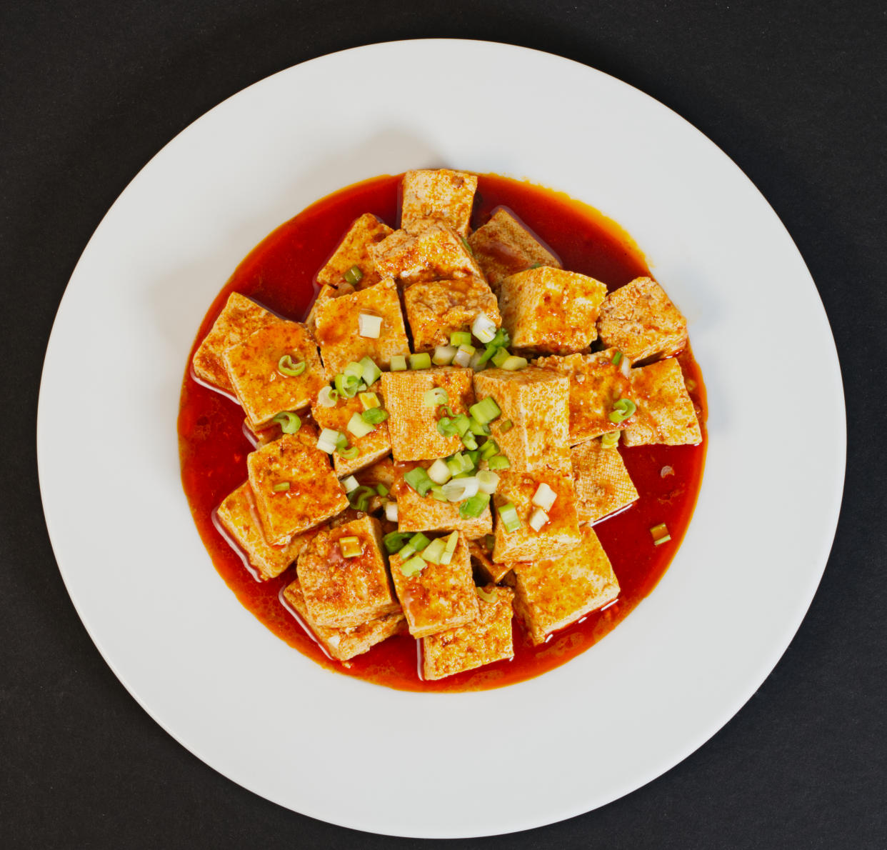 Spicy Tofu with red sauce in a white dish, black background, top view